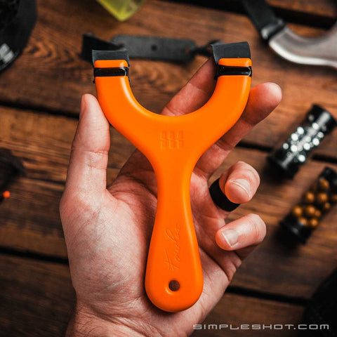 Orange Hornet slingshot held in hand showing the thin flat Fowler frame
